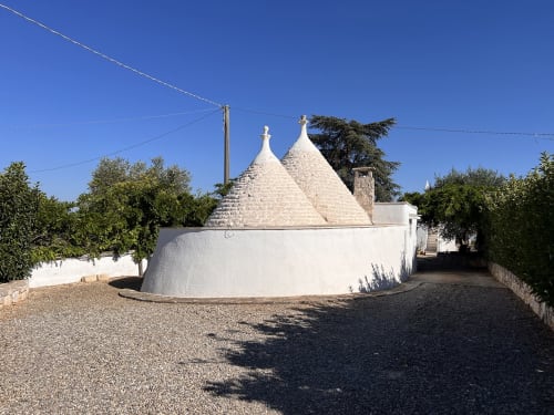 Villa trullo tradizionale imbiancata con tetto conico in pietra a Ostuni, Italia, caratterizzata da vialetto in ghiaia e atmosfera mediterranea