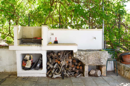 Cucina esterna con grill e deposito di legna da ardere nella villa Pietra & Luce a Ostuni, Italia, circondata da una lussureggiante vegetazione