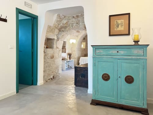 Porta e armadio turchese nell'ingresso di una villa a Ostuni con arco in pietra che conduce alla camera da letto