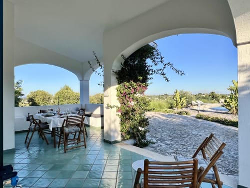 Area pranzo in terrazza ombreggiata con pergola bianca ad arco presso la villa Pietra & Luce a Ostuni, affacciata su giardino e campagna