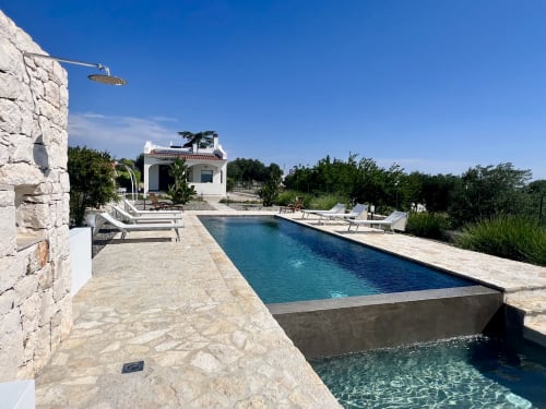 Piscina di lusso della villa Pietra & Luce a Ostuni, Italia con lettini, edificio in pietra e paesaggio mediterraneo