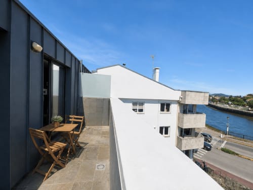Terraza del hotel Holibai en Baiona con mobiliario de madera, arquitectura moderna y vistas al frente marítimo