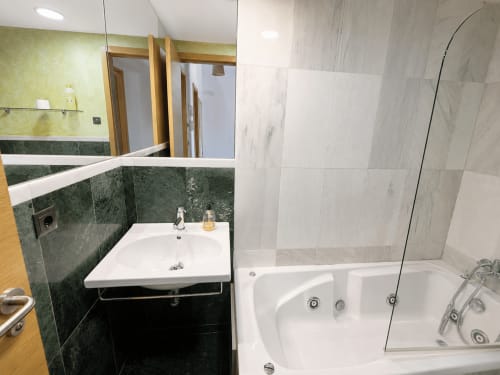 Baño moderno del hotel Holibai en Baiona con detalles en azulejos verdes, lavamanos blanco y ducha con cristal