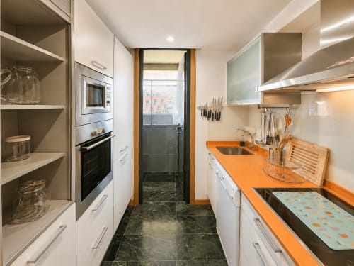 Moderna cocina del hotel Holibai en Baiona con muebles blancos, encimera naranja, electrodomésticos acero inoxidable y vistas a la ciudad