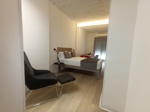 Dormitorio moderno en apartamento El Rincón de Sevilla con cama, sillón negro y suelo de madera clara