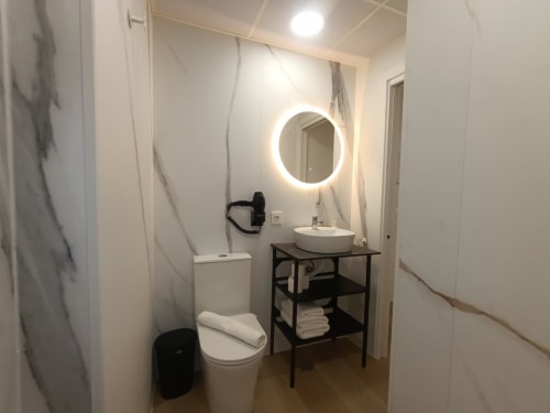 Baño moderno del apartamento El Rincón de Sevilla con espejo circular iluminado, lavabo redondo blanco, inodoro y detalles en negro