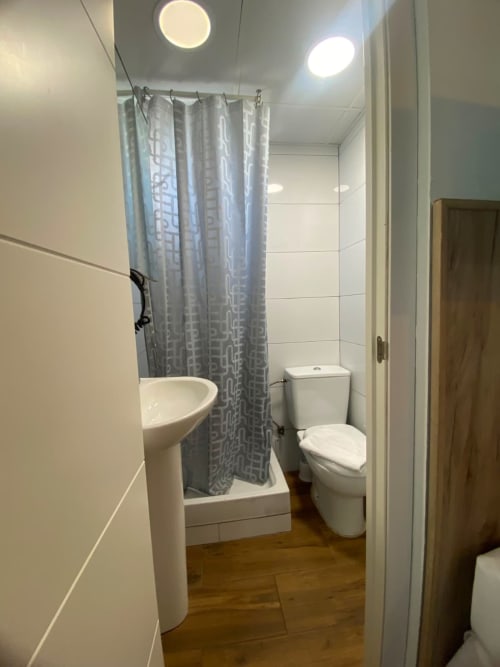 Baño moderno en apartamento El Rincón de Sevilla con lavabo de pedestal, inodoro, ducha con cortina gris y techo circular