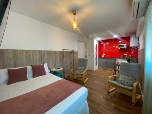 Moderno apartamento estudio en Sevilla con cama, cocina americana con azulejo rojo, suelos de madera y zona de estar