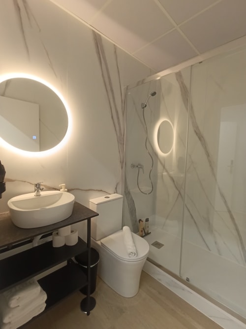 Baño moderno del apartamento El Rincón de Sevilla con espejo redondo iluminado, lavabo blanco, inodoro y ducha