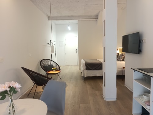 Moderno apartamento estudio en El Rincón de Sevilla con sala, cama, TV, sillas negras y cocina en San Juan de