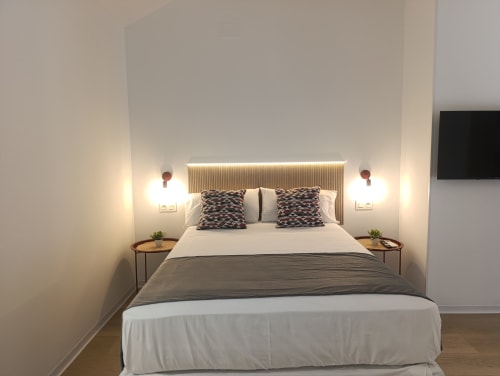 Moderna habitación en El Rincón de Sevilla con cama queen, iluminación de pared y pisos de madera en San Juan de Aznalfarache