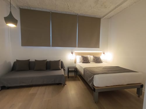 Dormitorio moderno en El Rincón de Sevilla con cama, sofá, suelo de madera e iluminación contemporánea en apartamento sevillano