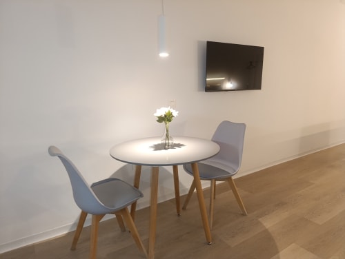Comedor moderno en apartamento El Rincón de Sevilla con mesa redonda, sillas grises, televisor y flores frescas