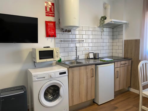 Cocina moderna en apartamento de Sevilla con lavadora, microondas, estufa, fregadero y azulejos blancos