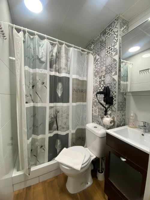 Baño moderno en el apartamento El Rincón de Sevilla con accesorios blancos, cortina de ducha con temática natural y tocador oscuro