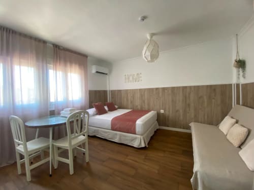 Espacioso dormitorio en apartamento de Sevilla con suelo de madera, cama queen, sofá, zona de escritorio y paredes revestidas en madera