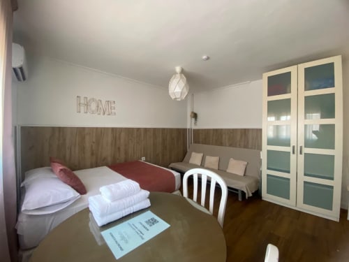Moderno dormitorio en apartamento de Sevilla con cama, sofá, lámpara colgante geométrica y detalles en madera cerca del centro histórico