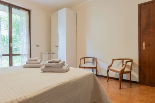 Ampia camera da letto dell'Hotel Prince Garda a Salò con letto, sedie in legno, armadio bianco e porte con vista sul giardino