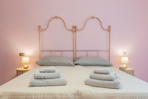 Camera elegante dell'Hotel Prince Garda a Salò con letto in ottone decorato, cuscini grigi, asciugamani arrotolati e pareti rosa