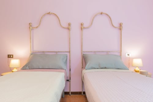Due letti singoli con testiere in ottone presso l'hotel Prince Garda a Salò, pareti rosa, lampade da comodino