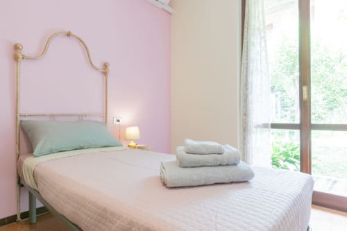 Camera luminosa all'hotel Prince Garda di Salò con pareti rosa, letto in ottone e asciugamani piegati sul letto