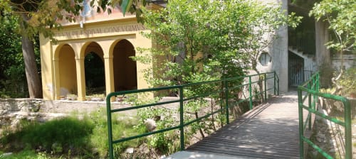 Edificio in pietra gialla con arcate dell'hotel Prince Garda a Salò, Italia, circondato da ringhiere in legno verde e vegetazione lussureggiante.