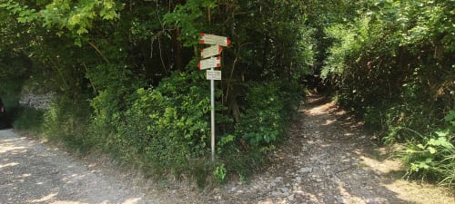 Palo segnaletico con cartelli direzionali rossi e bianchi su sentiero boschivo presso Prince Garda, Salò Italia