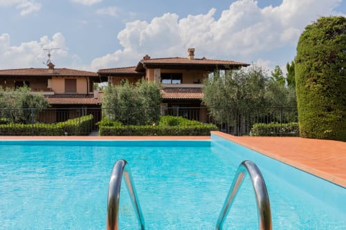 Piscina con scala metallica dell'Hotel Prince Garda a Salò, Italia, con vista su villa in terracotta