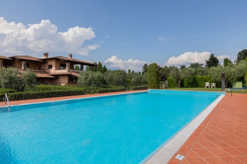 Ampia piscina scintillante blu all'hotel Prince Garda di Salò, con terrazza in cotto e villa toscana sullo sfondo