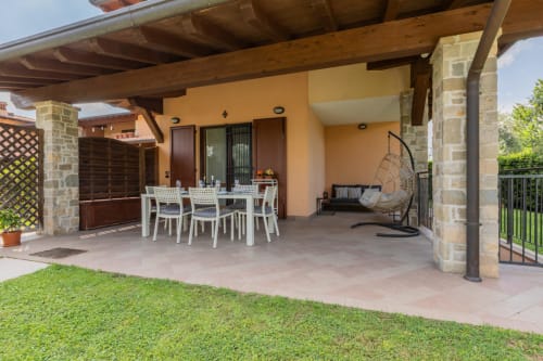 Patio Prince Garda a Salò con tavolo da pranzo, sedia sospesa e edificio in pietra gialla sotto pergolato in legno