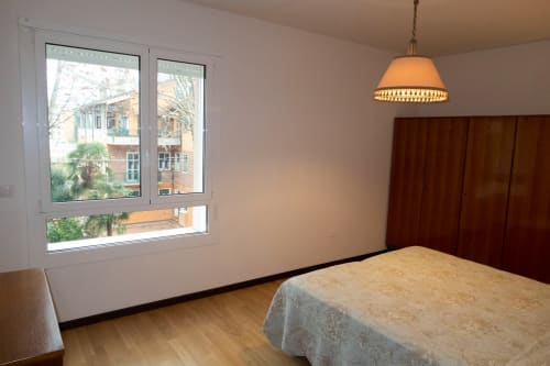 Bright bedroom at Casa di Cinti in Pianoro with hardwood floors, bed, dark wood wardrobe, pendant light, and large window