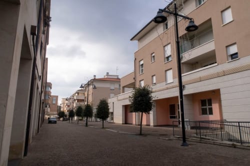 Inner courtyard at Casa di Cinti in Pianoro, Italy, featuring modern residential building with manicured trees and street