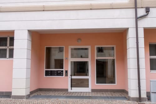 Casa di Cinti apartment entrance in Pianoro with coral-pink facade, white trim, and glass doors overlooking inner courtyard