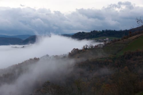 Paesaggio di valle nebbiosa a Casa di Cinti con colline ondulate, fitti boschi e nuvole drammatiche in Italia