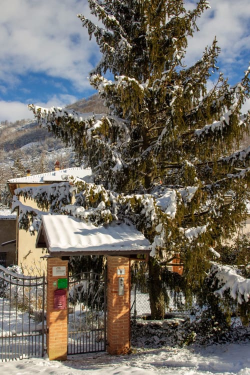 Snow-covered gatehouse at Casa di Cinti B&B in Italian mountains with frosted trees