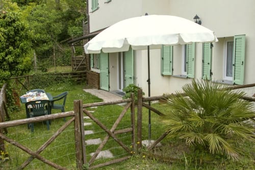 Casa di Cinti garden patio with white umbrella, wooden gates, and green shuttered rooms in Italian countryside