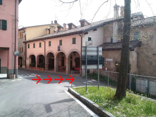 Casa di Cinti courtyard with pink Renaissance building, arches, and red directional arrows in Italian town