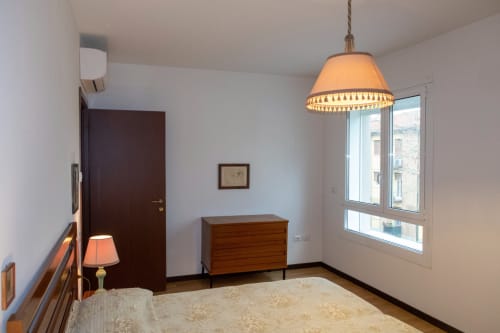 Casa di Cinti bedroom with wooden door, pendant lamp, dresser, and window overlooking Italian street