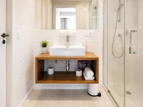 Baño moderno en Holibai, Baiona, con tocador de madera, lavamanos blanco y ducha con cristalería