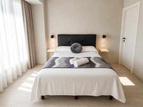 Moderno dormitorio del hotel Holibai en Baiona con cabecero negro, ropa de cama blanca y decoración minimalista