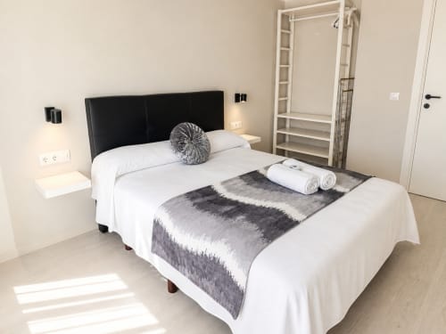 Dormitorio moderno del hotel Holibai en Baiona con cabecero negro, ropa de cama blanca y manta gris estampada