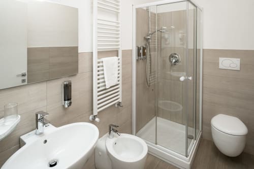 Bagno moderno e accessibile dell'Hotel Villa Mary con lavabo bianco, bidet, wc e doccia con divisorio in vetro su piastrelle beige