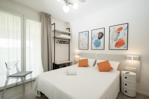 Camera da letto moderna all'Hotel Villa Mary con biancheria bianca, dettagli arancioni, quadri e balcone con vista giardino a Santa Maria
