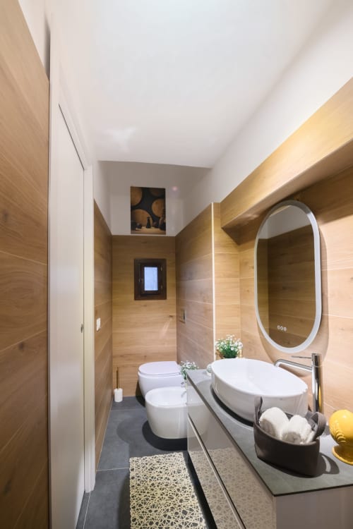 Bagno moderno dell'hotel Almatros a Sulmona con rivestimento in legno, specchio ovale, sanitari bianchi e design contemporaneo