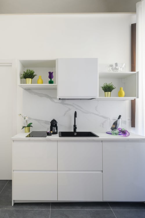 Cucina bianca moderna dell'hotel Almatros di Sulmona, con rivestimento in marmo, ripiani sospesi e piante decorative