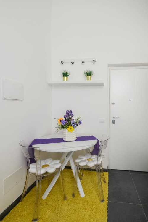 Appartamento Giallo all'hotel Almatros di Sulmona con zona pranzo moderna, tavolo bianco, sedie trasparenti e fiori freschi