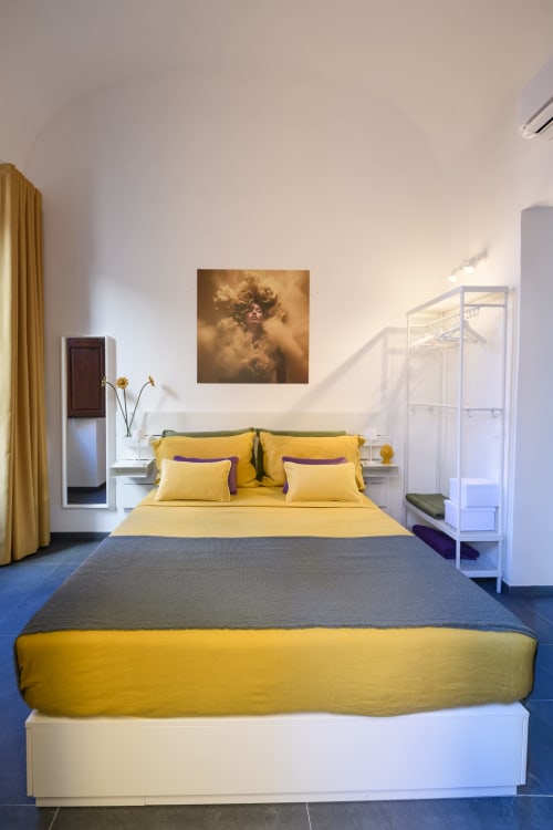 Camera gialla dell'hotel Almatros a Sulmona con letto giallo e accenti viola, comodini bianchi e opere d'arte dorate