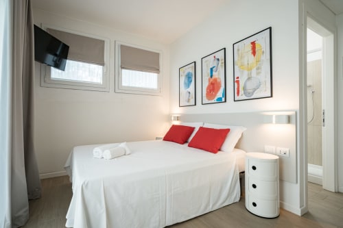 Camera matrimoniale moderna all'Hotel Villa Mary con letto bianco, cuscini rossi, opere d'arte astratta, TV e arredi contemporanei
