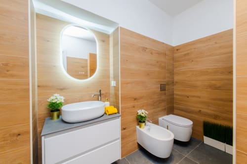 Moderno bagno dell'Appartamento Green all'hotel Almatros di Sulmona, con pareti in legno, specchio ovale illuminato e lavabo bianco