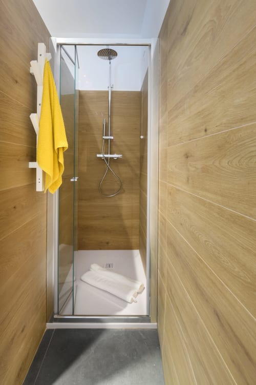 Moderno box doccia nell'Apartment Green dell'hotel Almatros di Sulmona, con piastrelle effetto legno e asciugamano giallo